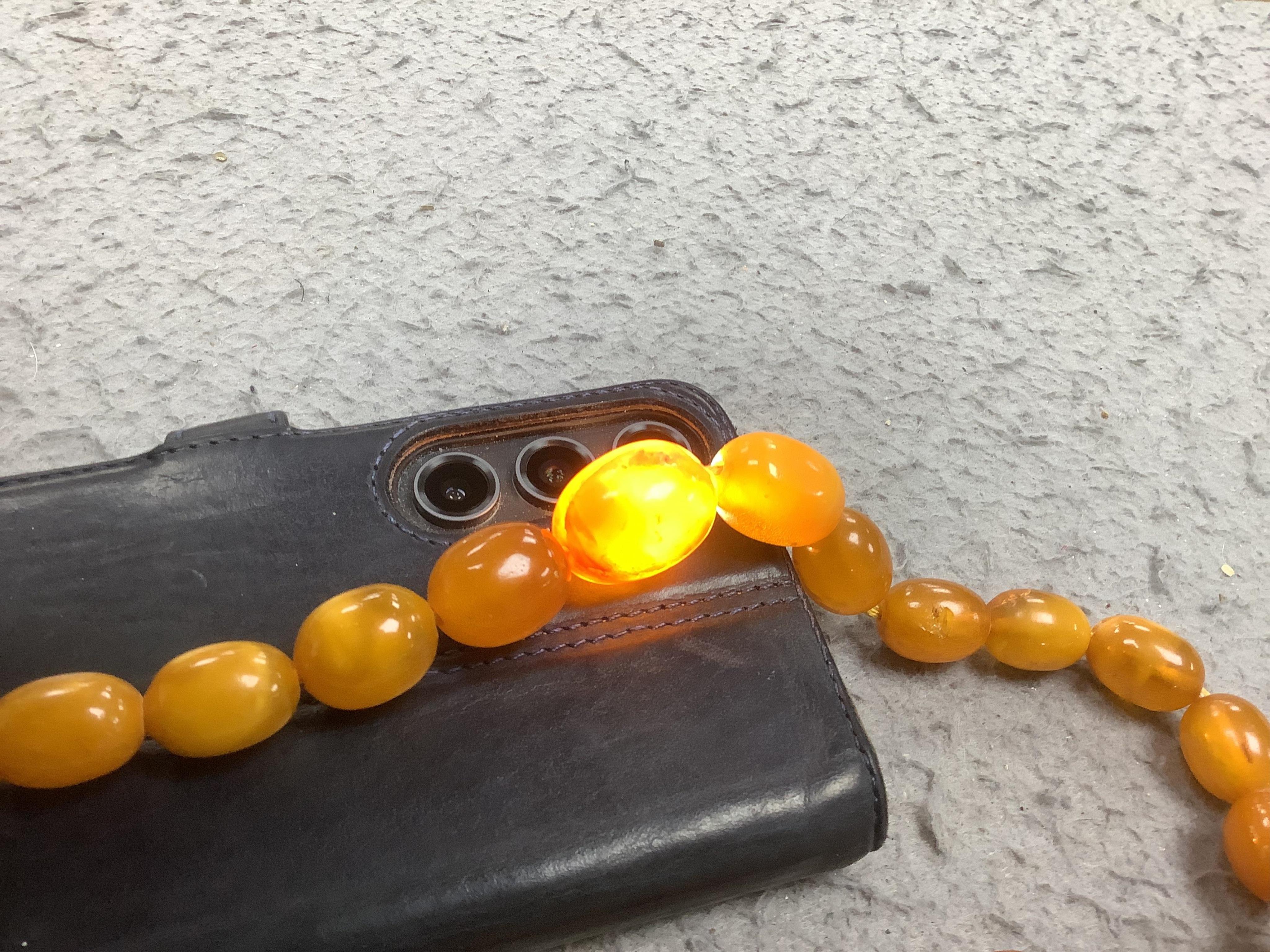 A single strand graduated oval amber bead necklace (a.f.), 90cm, gross weight 72 grams and three odd beads and an earring. Condition - poor